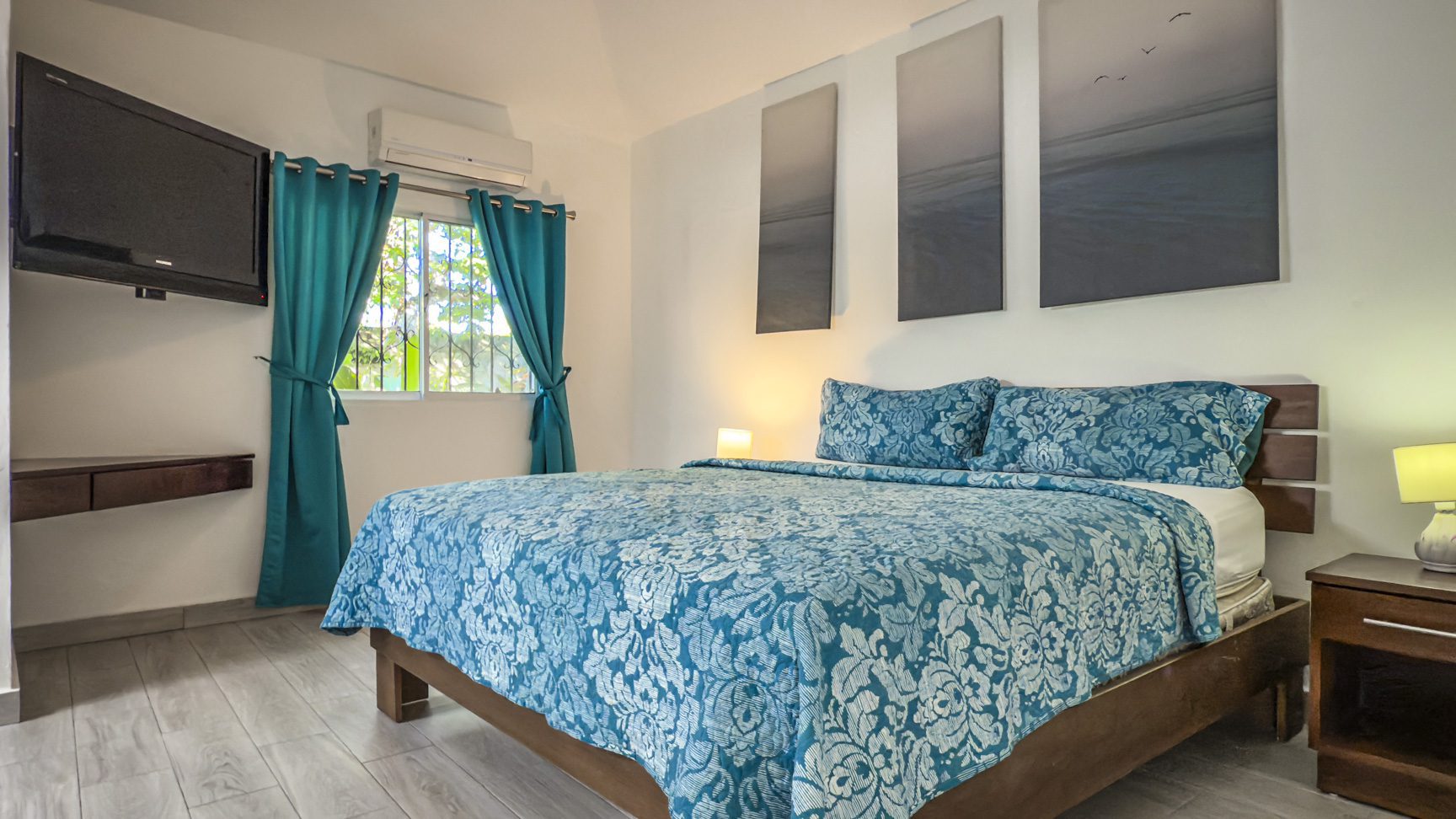 buyDRproperty Bedroom with blue floral bedding, wall art, and a TV. Modern interior design, bright and airy. Sosua Real Estate