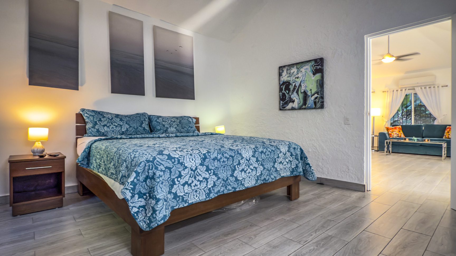 buyDRproperty Bedroom with blue floral bedding, modern art, and open doorway to living room. Sosua Real Estate
