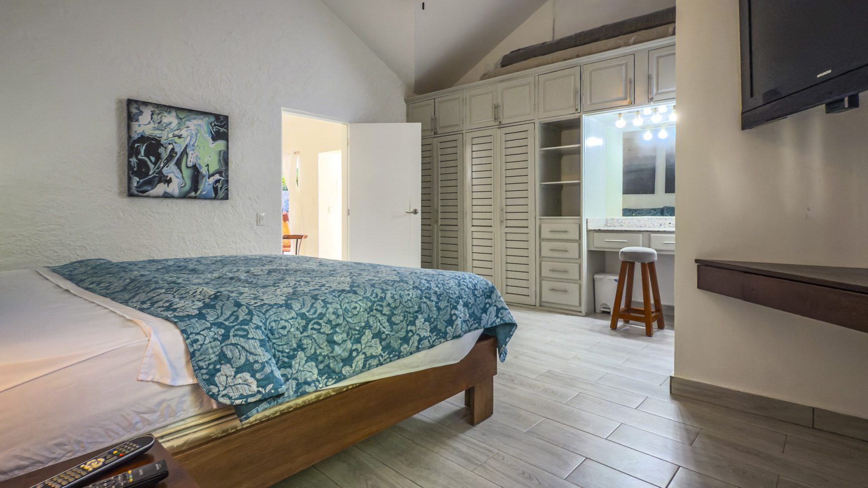 buyDRproperty Bedroom with blue patterned bedding, built-in wardrobe, vanity area, and light wood-look flooring. Sosua Real Estate