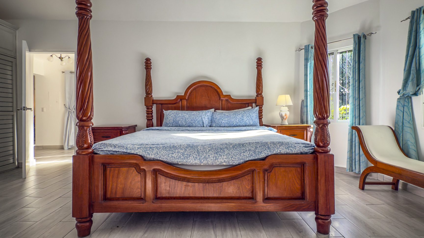 buyDRproperty Ornate four-poster bed in a bright bedroom with wooden floors and blue curtains. Sosua Real Estate