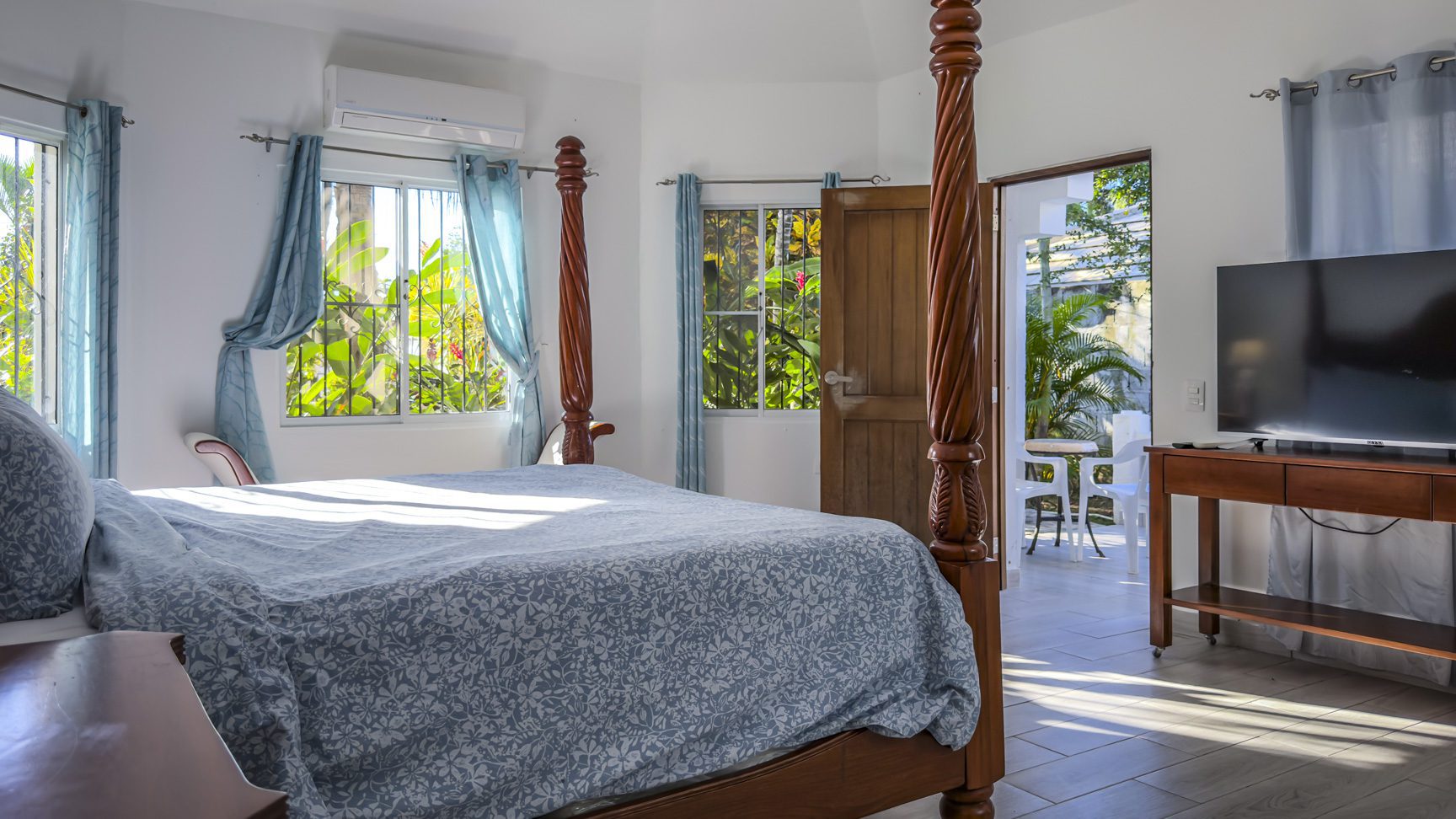 buyDRproperty Bright bedroom with four-poster bed, blue curtains, and open door to a sunny patio. Sosua Real Estate