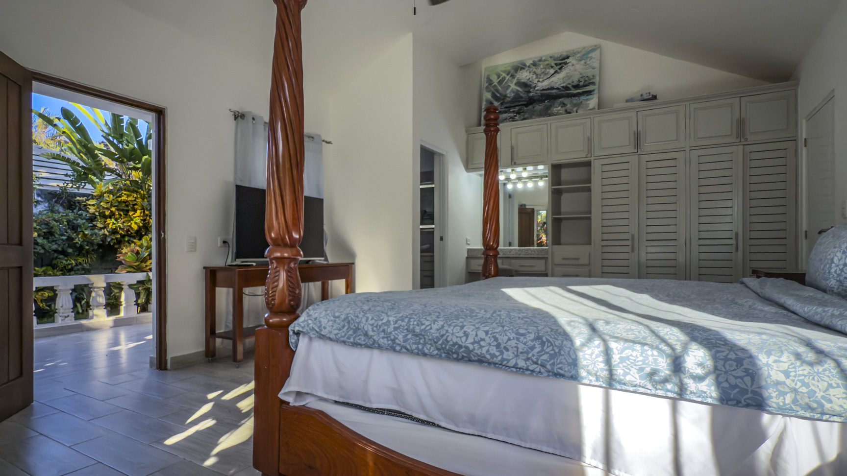 buyDRproperty Bright bedroom with four-poster bed, built-in wardrobe, and balcony view of lush tropical garden Sosua Real Estate