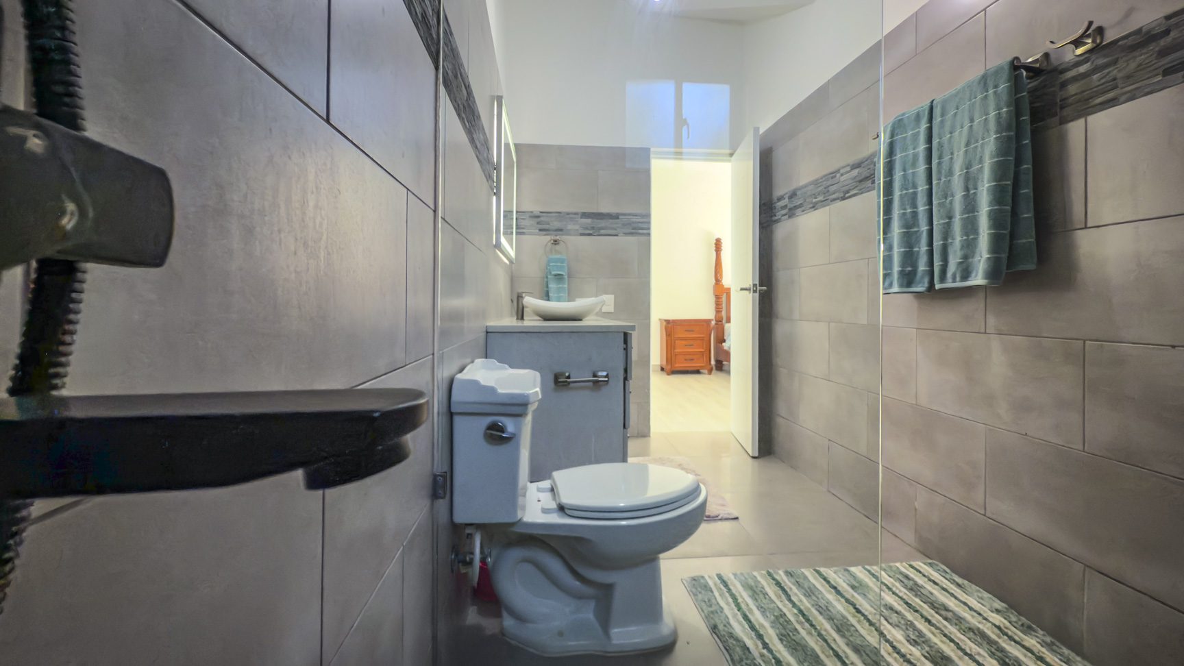 buyDRproperty Modern bathroom with gray tile, white toilet, sink, and a glimpse into a bedroom. Sosua Real Estate