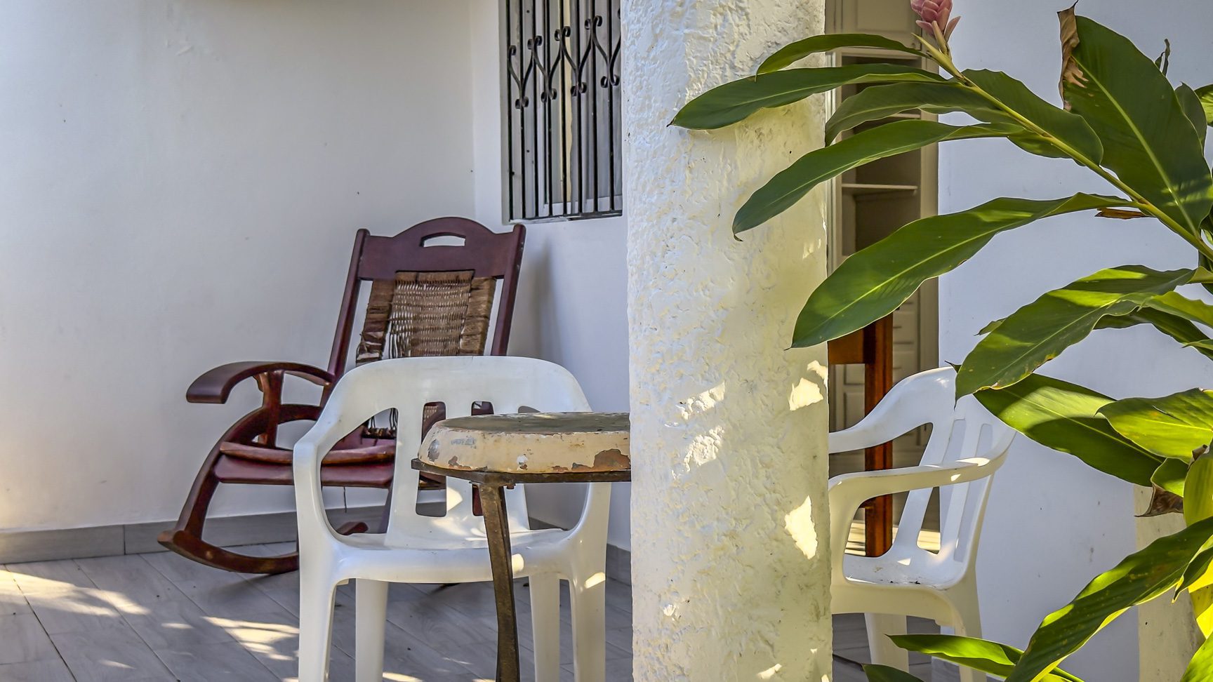 buyDRproperty Patio scene with rocking chair, white plastic chairs, and tropical plants; outdoor living. Sosua Real Estate