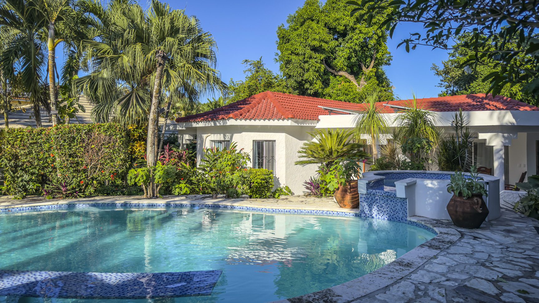buyDRproperty Tropical villa with a turquoise pool, red tile roof, and lush green landscaping. Sosua Real Estate