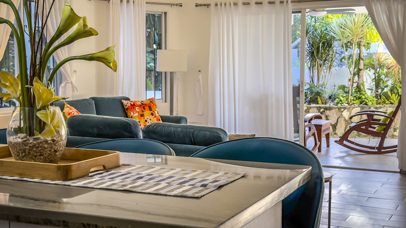 buyDRproperty Bright living room with blue sofa, tropical flowers, and patio leading to a garden. Sosua Real Estate