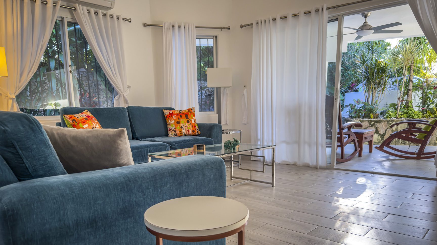 buyDRproperty Bright living room with blue sofas, open patio doors leading to a tropical garden. Sosua Real Estate