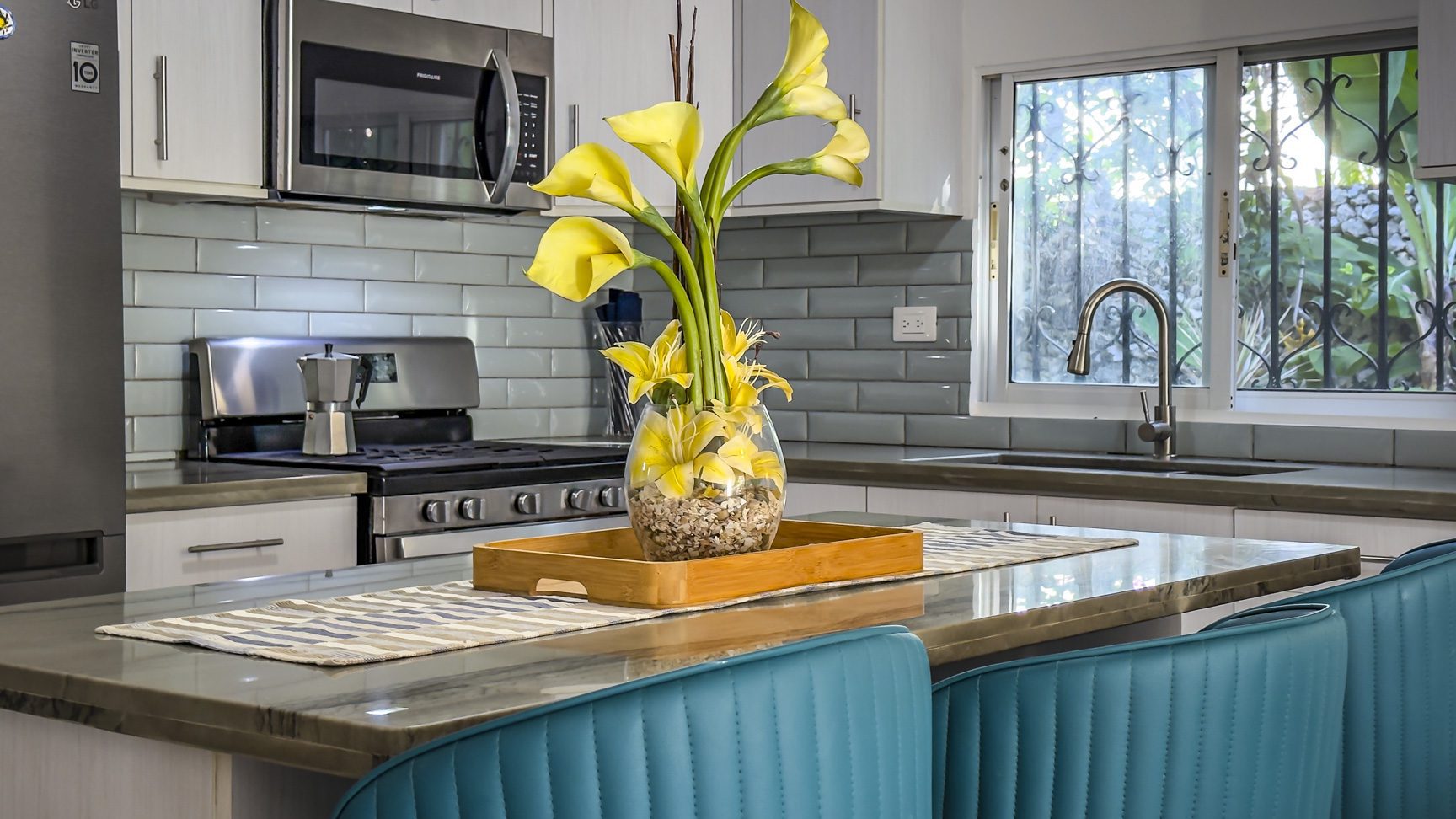 buyDRproperty Modern kitchen with gray subway tile backsplash, stainless steel appliances, and yellow calla lilies in a glass vase. Sosua Real Estate