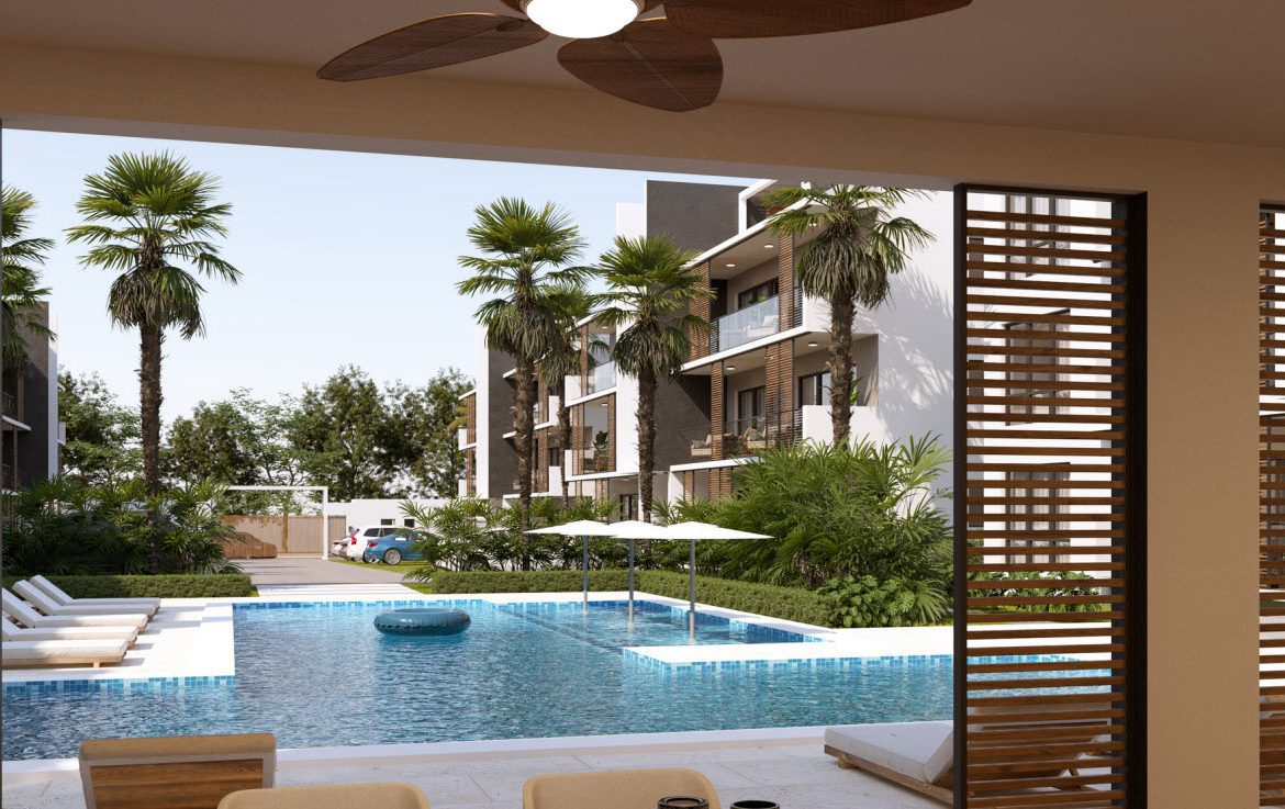 buyDRproperty Luxury resort pool with lounge chairs and palm trees, seen from a condo balcony. Zocalo Group logo visible. Sosua Real Estate