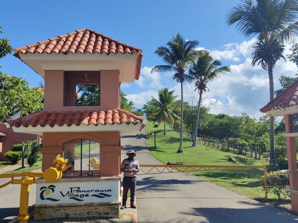 buyDRproperty Panorama Village entrance in Sosua, Dominican Republic, with security guard and palm trees. Sosua Real Estate