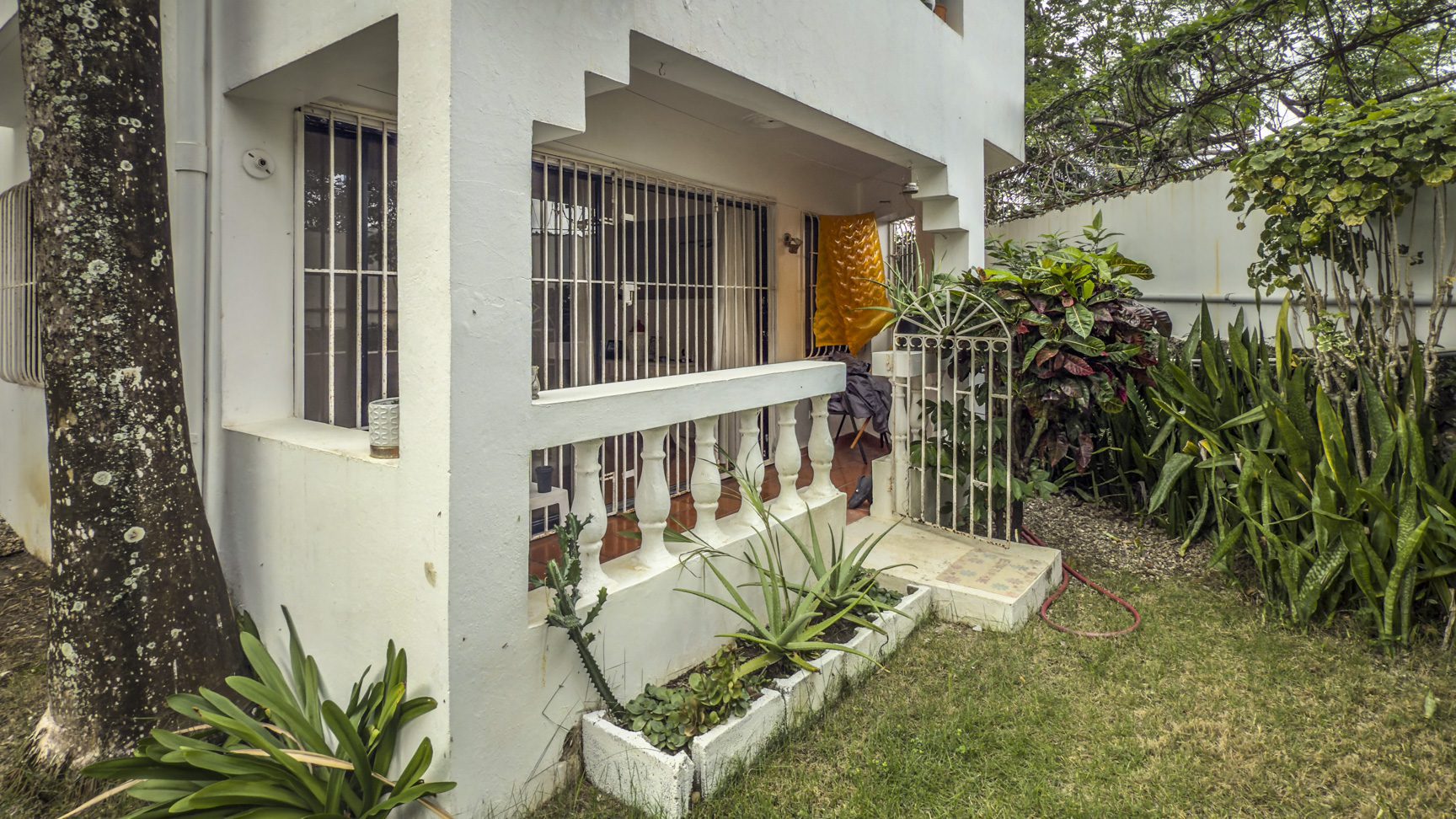 buyDRproperty Exterior view of a 2-bedroom house for sale in Sosúa, featuring a small garden and covered porch. Sosua Real Estate