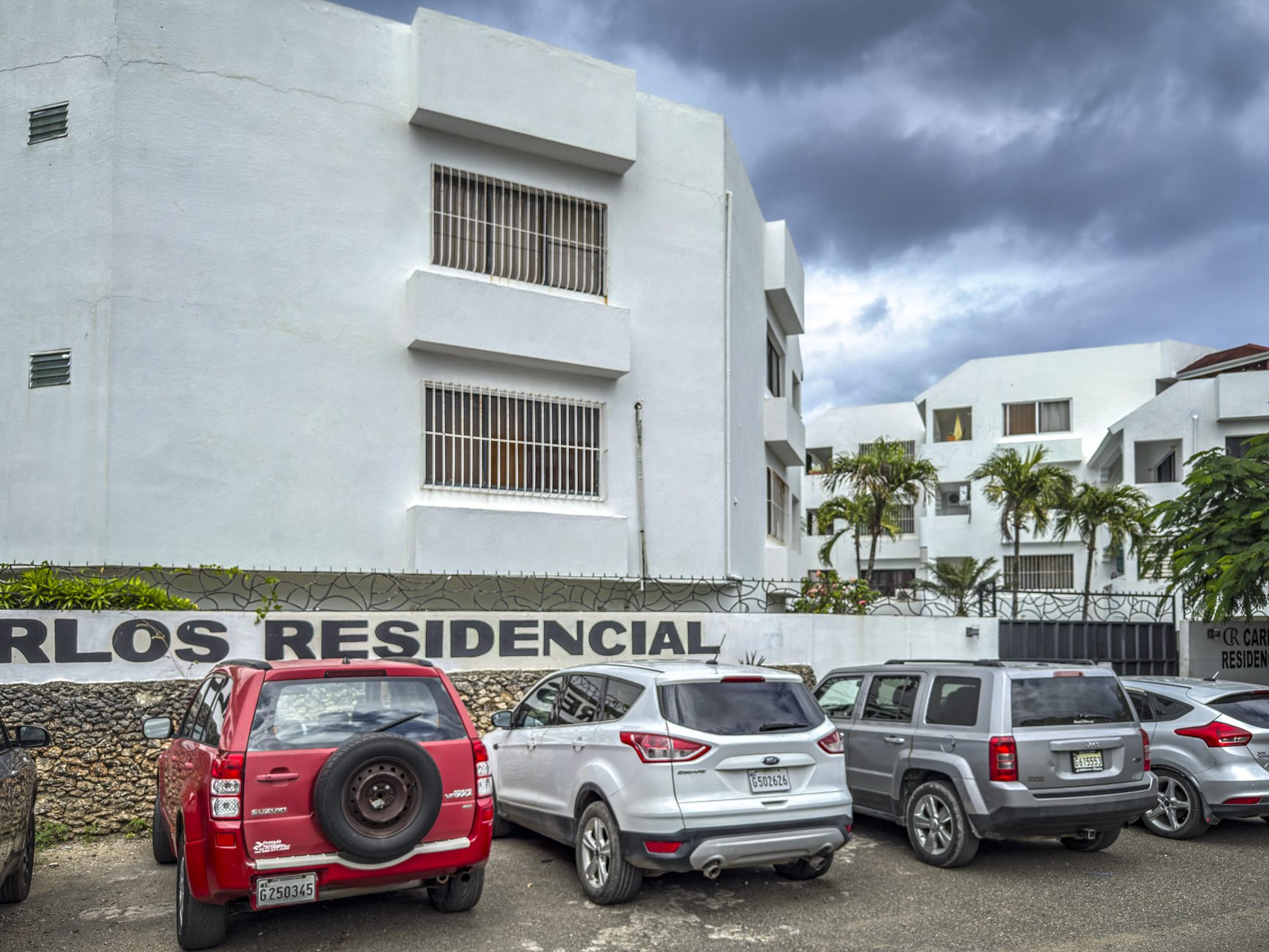 buyDRproperty Cars parked in front of Carlos Residencial, Sosúa. "Carlos Residencial" sign visible. Near playa. Sosua Real Estate