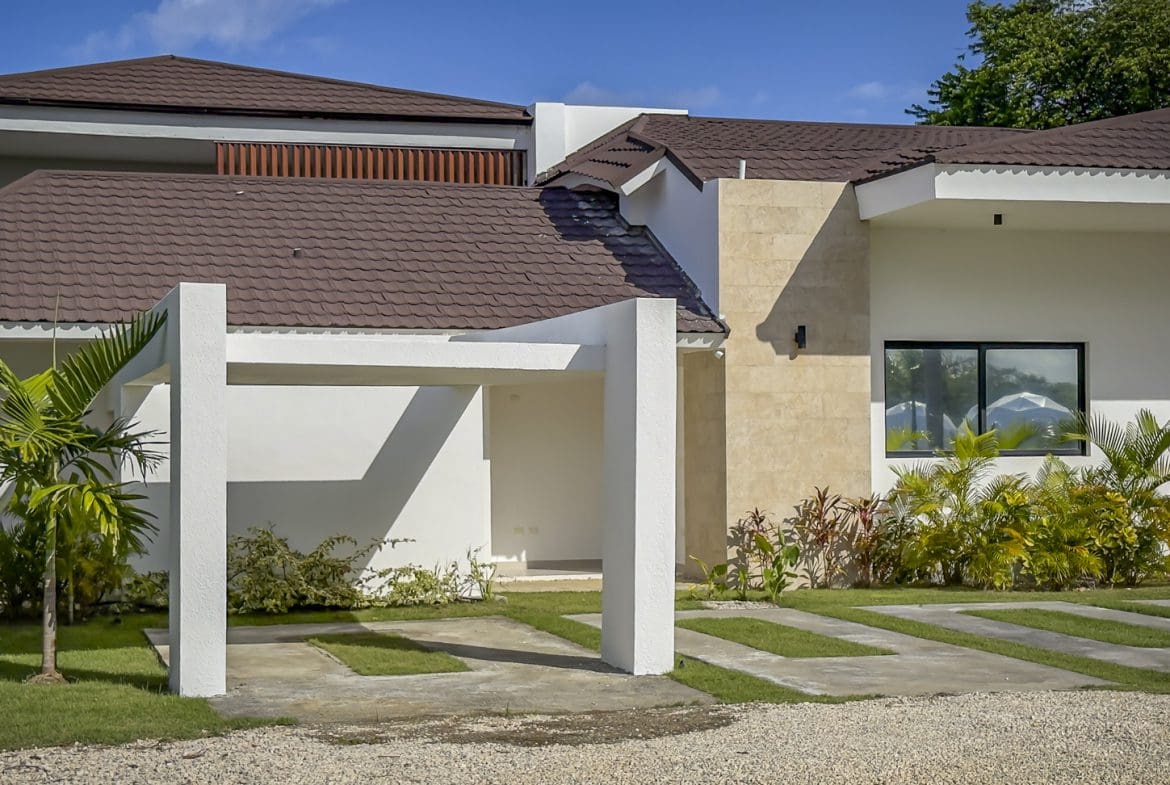 buyDRproperty Exterior of a luxury villa with a modern carport and lush landscaping. Sosua Real Estate