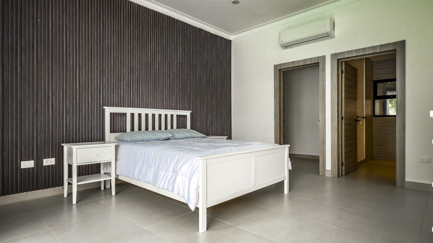 buyDRproperty Luxury villa bedroom with white bed and dark wood accent wall in Sosua Ocean Village. Sosua Real Estate