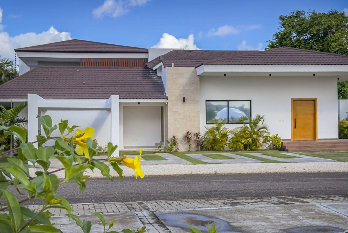 buyDRproperty Modern luxury villa with a brown roof and white exterior, palm trees, and blue sky. Sosua Real Estate