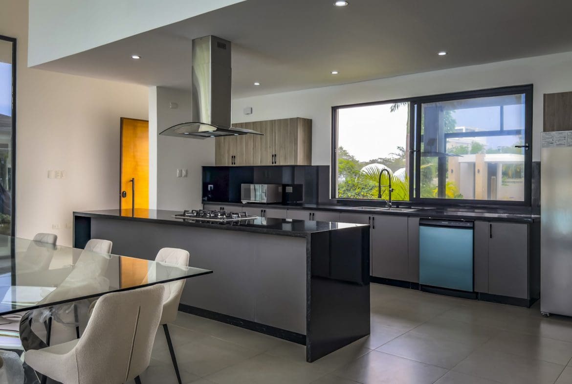 buyDRproperty Modern kitchen in a luxury villa with island, stainless steel appliances, and large window. Sosua Real Estate