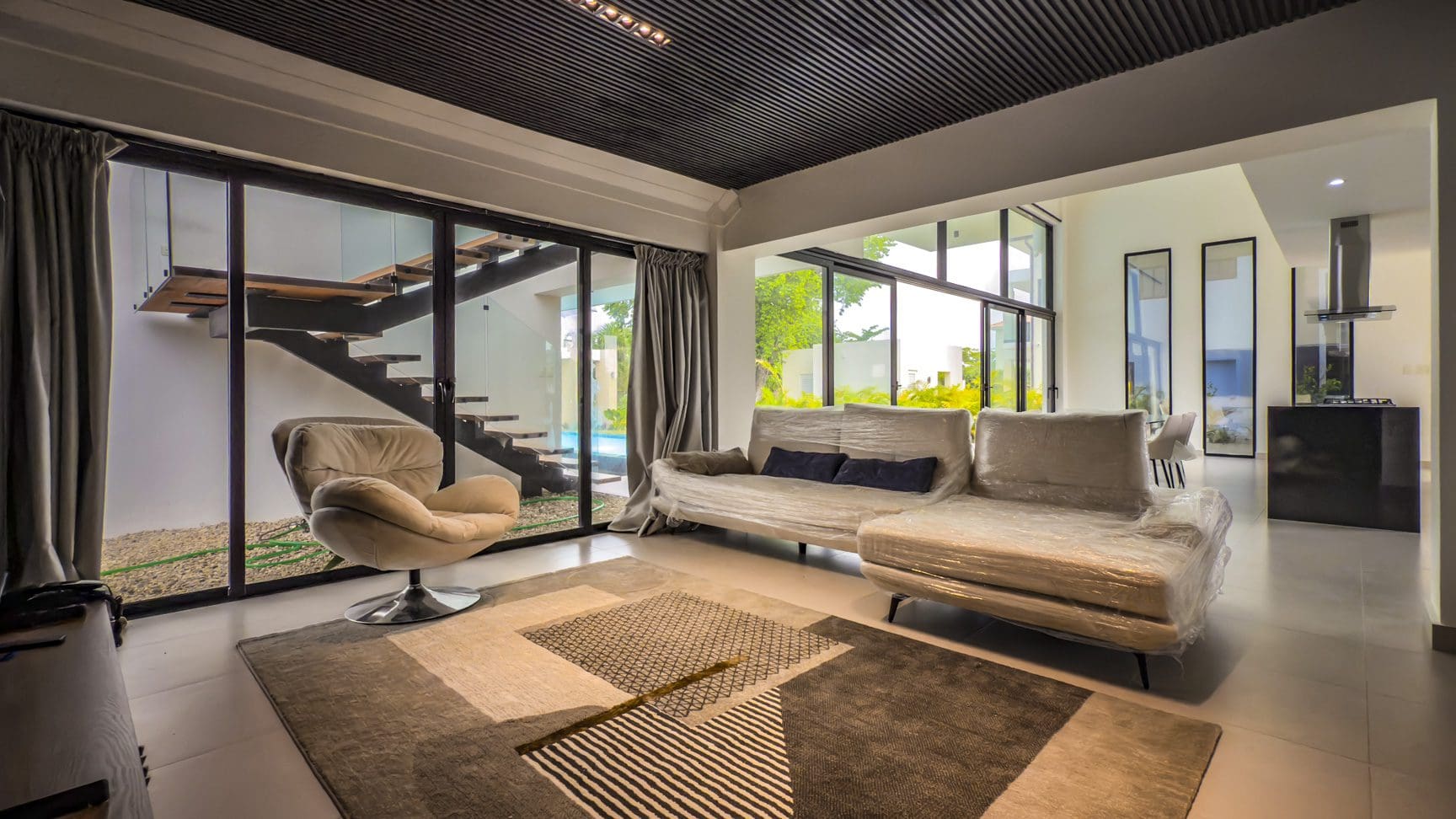 buyDRproperty Luxury villa interior with modern staircase, neutral tones, and large windows overlooking the pool. Sosua Real Estate