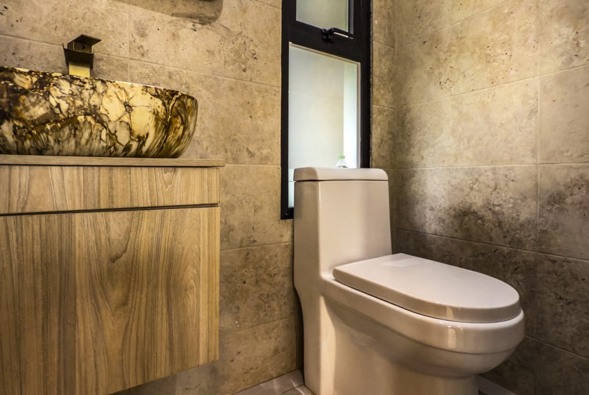 buyDRproperty Luxury villa bathroom with stone vessel sink and modern toilet, tiled wall. Sosua Real Estate