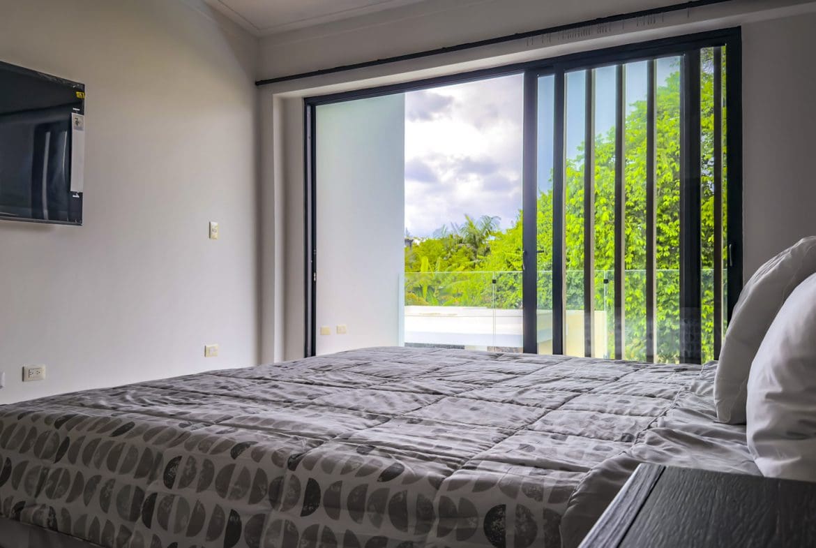 buyDRproperty Luxury villa bedroom with king bed and balcony overlooking lush greenery. Sosua Real Estate