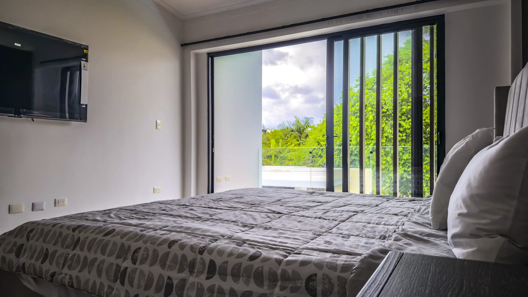 buyDRproperty Luxury villa bedroom with king bed and balcony overlooking lush greenery. Sosua Real Estate