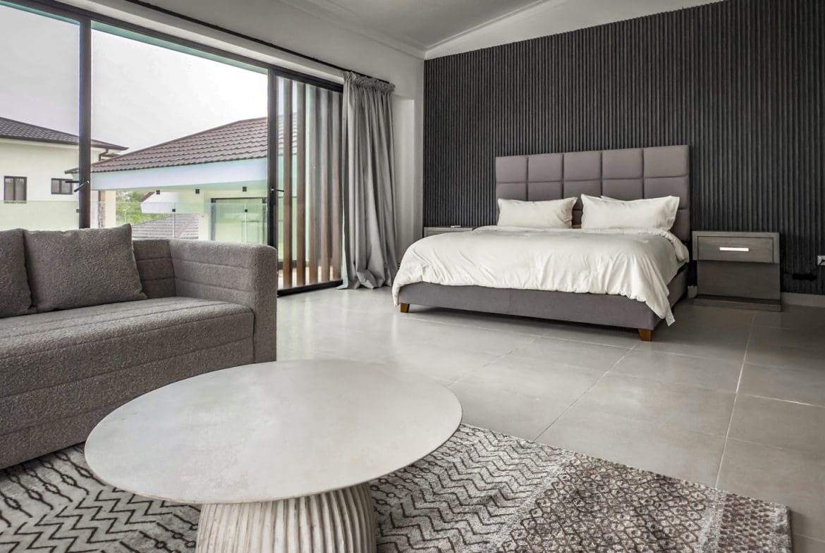 buyDRproperty Modern bedroom in a luxury villa with a gray sofa and large windows. Sosua Real Estate