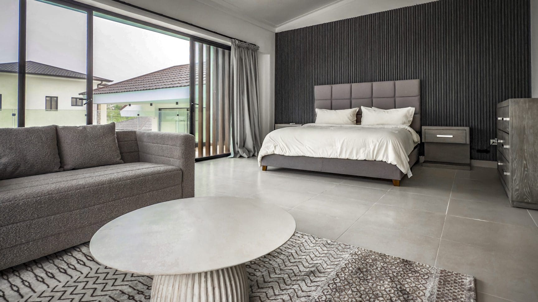 buyDRproperty Modern bedroom in a luxury villa with a gray sofa and large windows. Sosua Real Estate