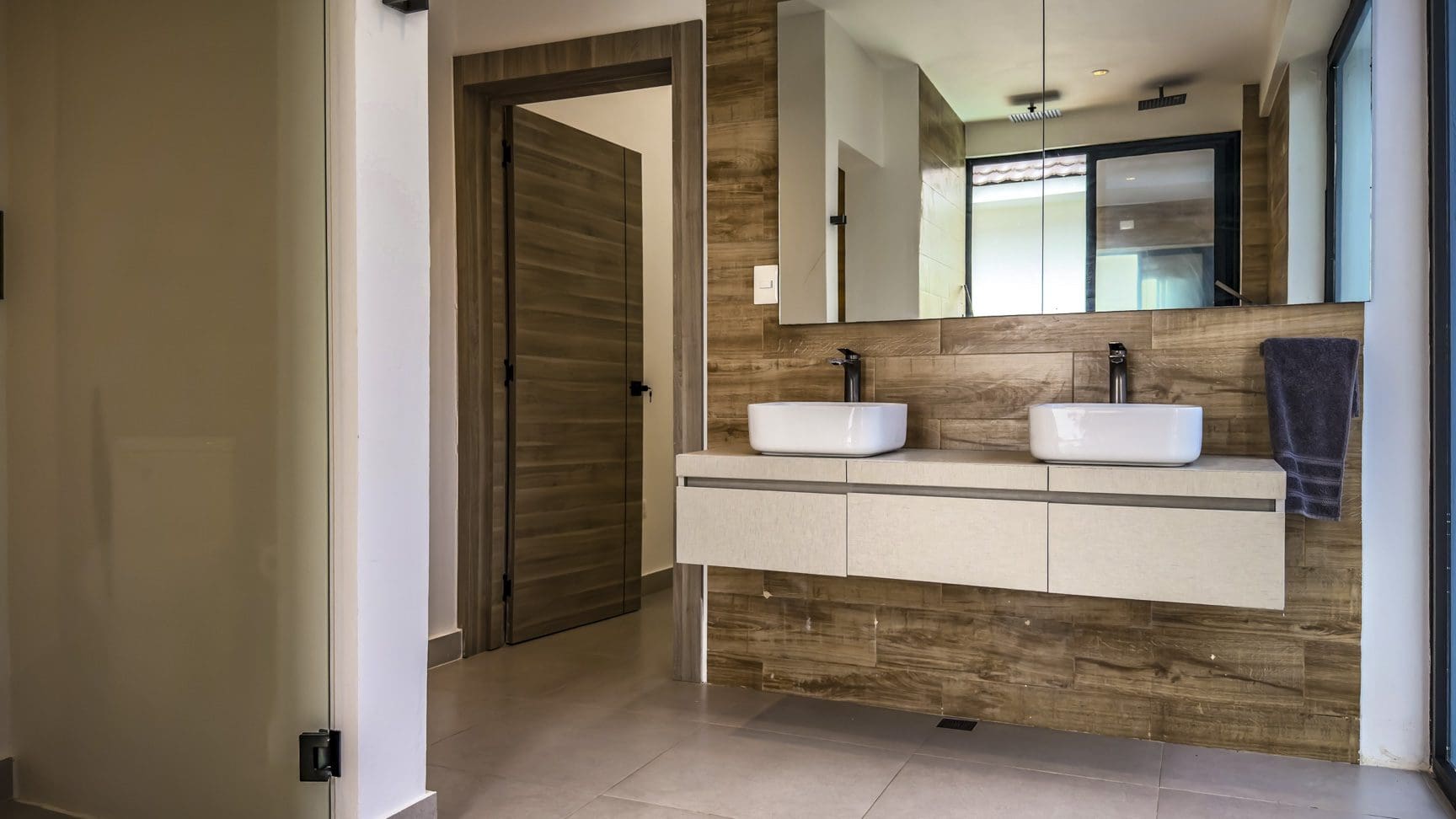 buyDRproperty Modern bathroom with double sinks and wood-look tile in a luxury Sosua villa. Sosua Real Estate