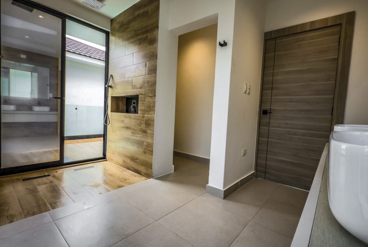 buyDRproperty Modern bathroom with glass shower, tiled walls, and doorway, showcasing luxury villa design. Sosua Real Estate