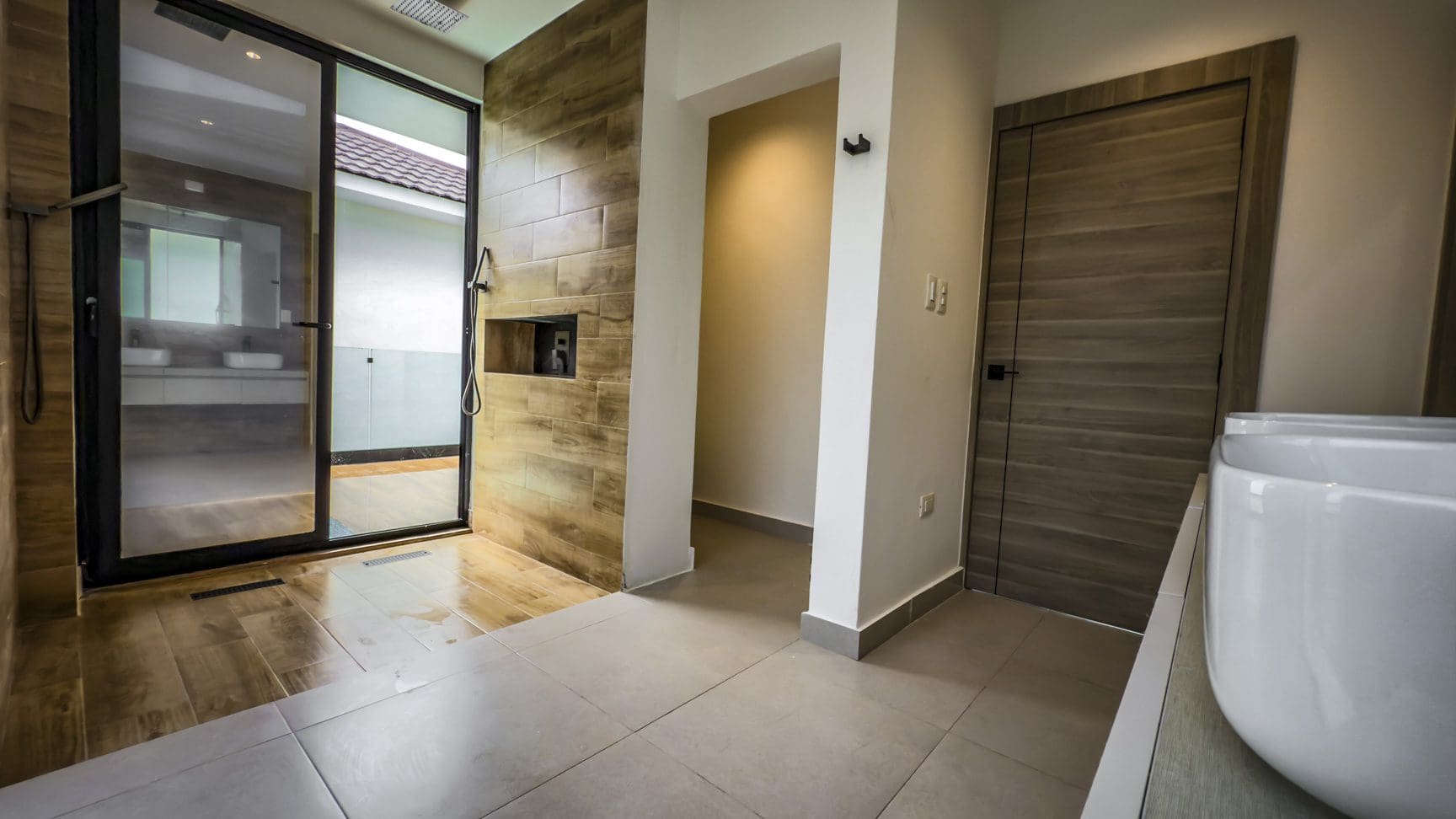 buyDRproperty Modern bathroom with glass shower, tiled walls, and doorway, showcasing luxury villa design. Sosua Real Estate