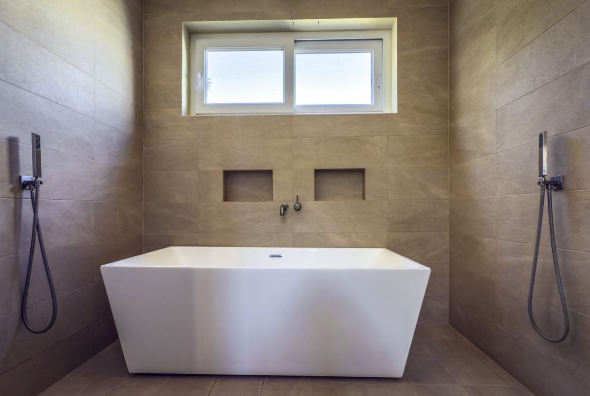 buyDRproperty Modern bathroom with white freestanding tub, neutral tile, and window. Sosua Real Estate