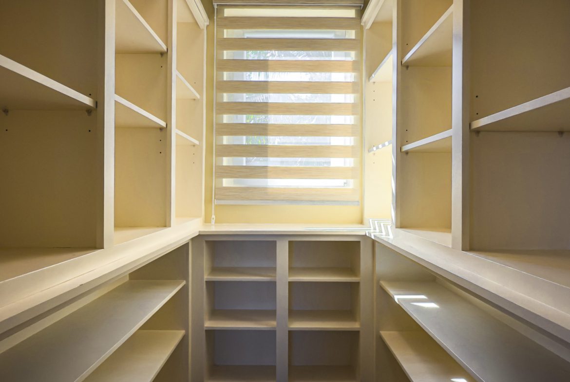 buyDRproperty Walk-in closet with built-in shelving and a window with blinds, showcasing villa interior. Sosua Real Estate