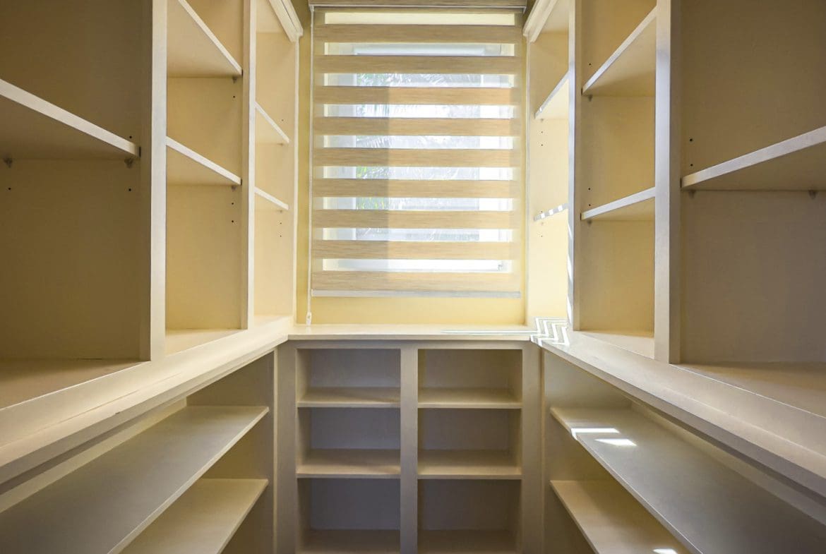 buyDRproperty Walk-in closet with built-in shelving and a window with blinds, showcasing villa interior. Sosua Real Estate