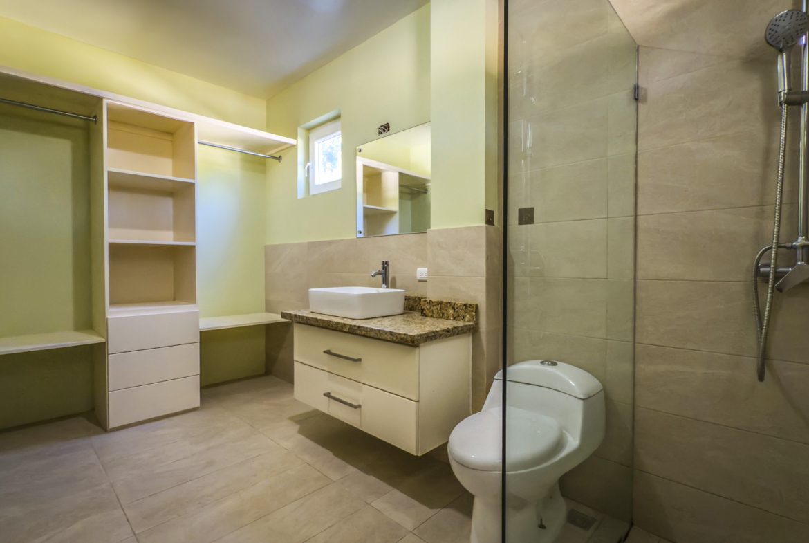 buyDRproperty Modern bathroom with shower, toilet, vanity, and open closet space in La Mulata villa. Sosua Real Estate