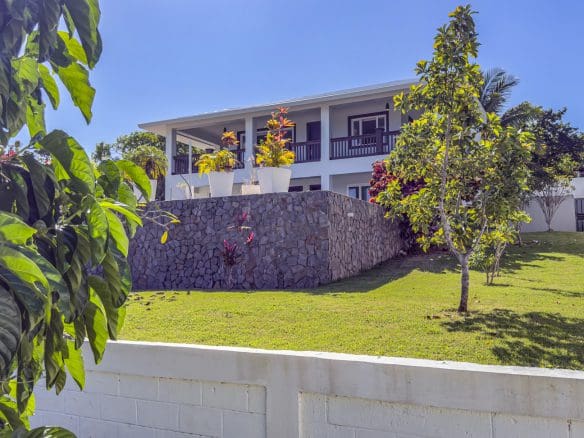 buyDRproperty La Mulata villa for sale: Three-bedroom house with stone foundation, balcony, and manicured lawn on a sunny day. Sosua Real Estate