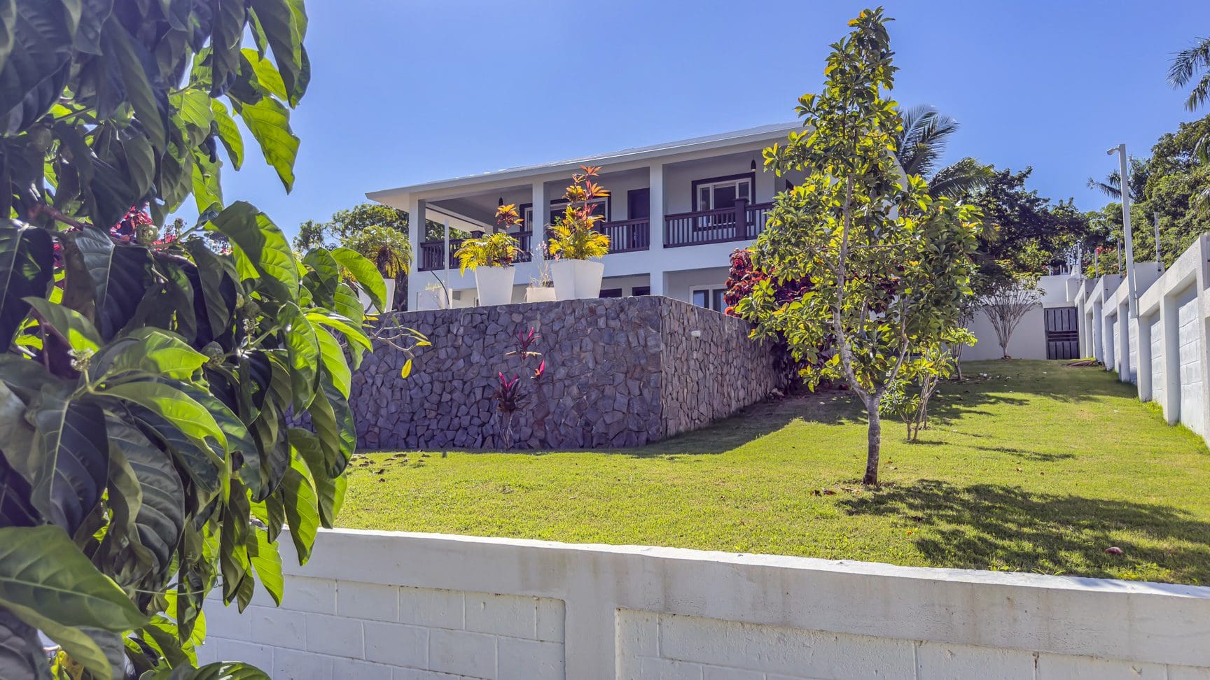 buyDRproperty La Mulata villa for sale: Three-bedroom house with stone foundation, balcony, and manicured lawn on a sunny day. Sosua Real Estate