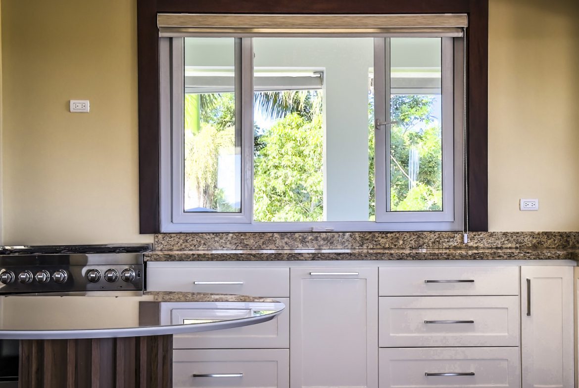 buyDRproperty Kitchen in La Mulata villa with white cabinets, granite countertops, and a window view of lush greenery. Sosua Real Estate