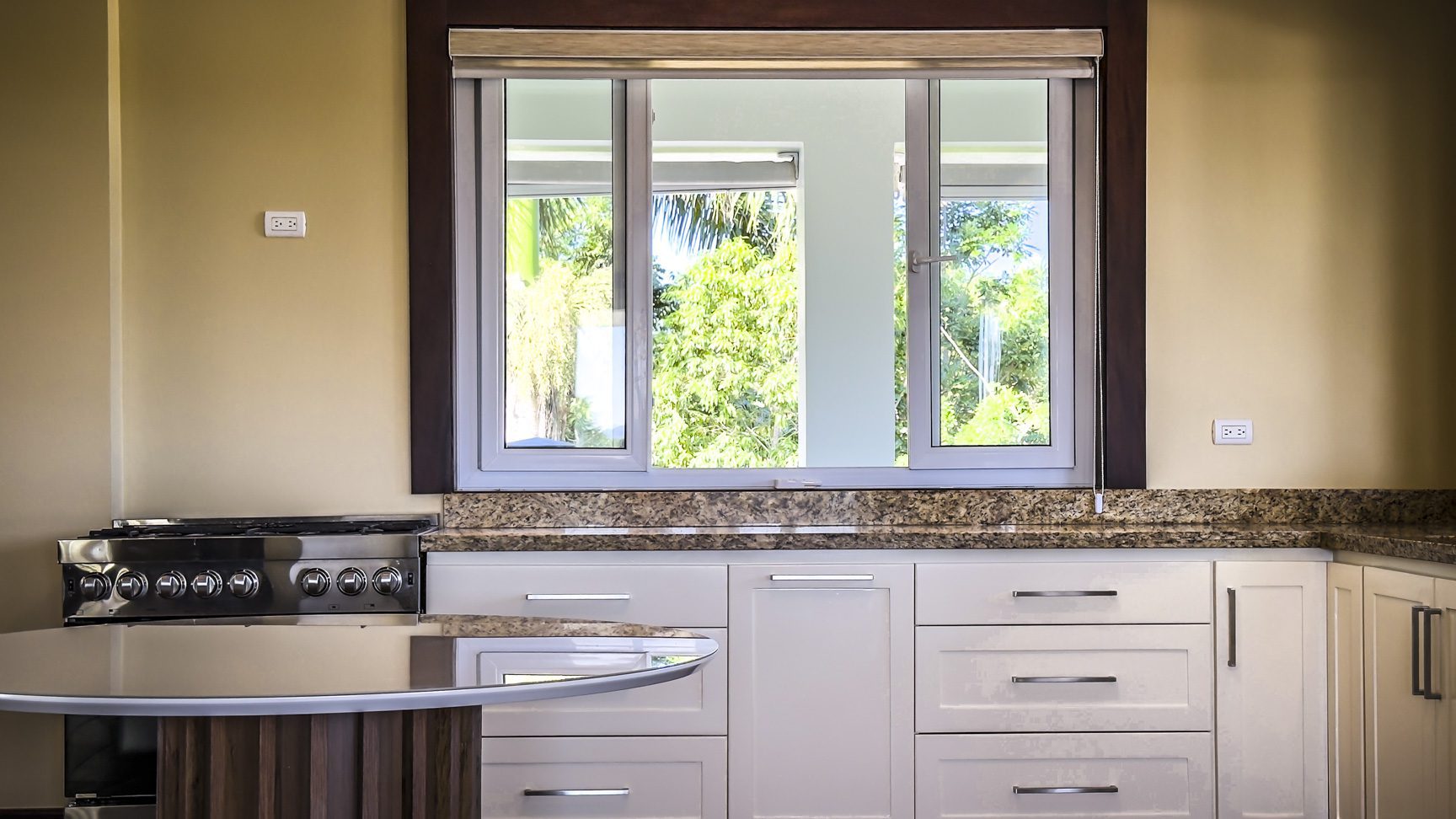 buyDRproperty Kitchen in La Mulata villa with white cabinets, granite countertops, and a window view of lush greenery. Sosua Real Estate