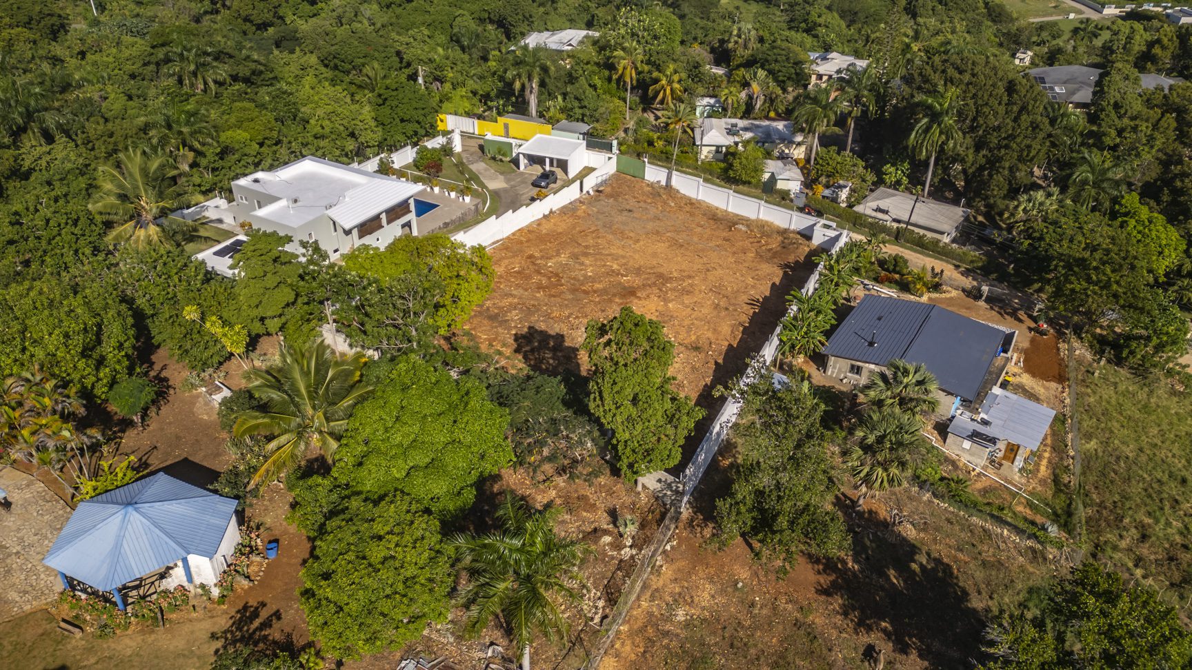 buyDRproperty Aerial view of a 3-bedroom villa for sale in La Mulata, Dominican Republic, surrounded by lush greenery and neighboring homes. Sosua Real Estate