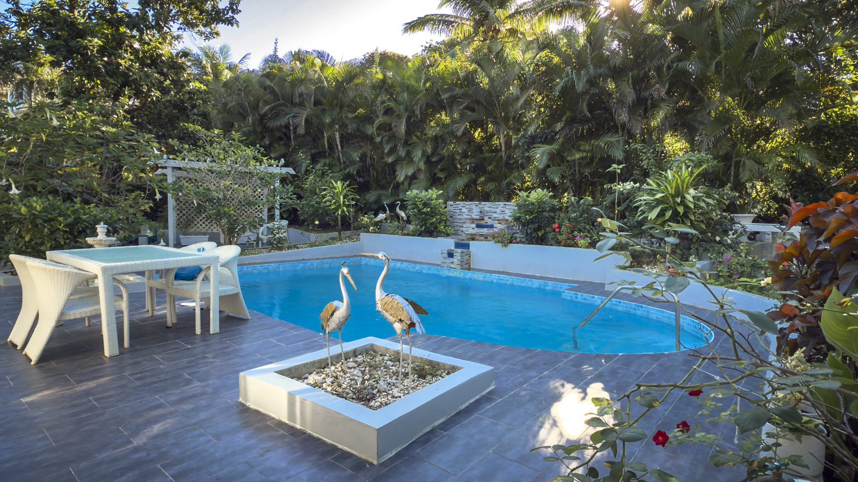 buyDRproperty Tropical villa pool with crane statues, lush garden, and waterfall feature. Sosua Real Estate
