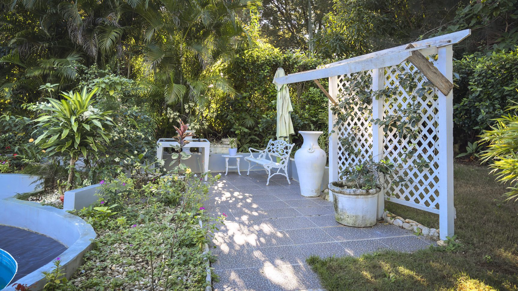 buyDRproperty Colibri villa garden with white pergola, bench, and tropical plants, creating a peaceful oasis. Sosua Real Estate