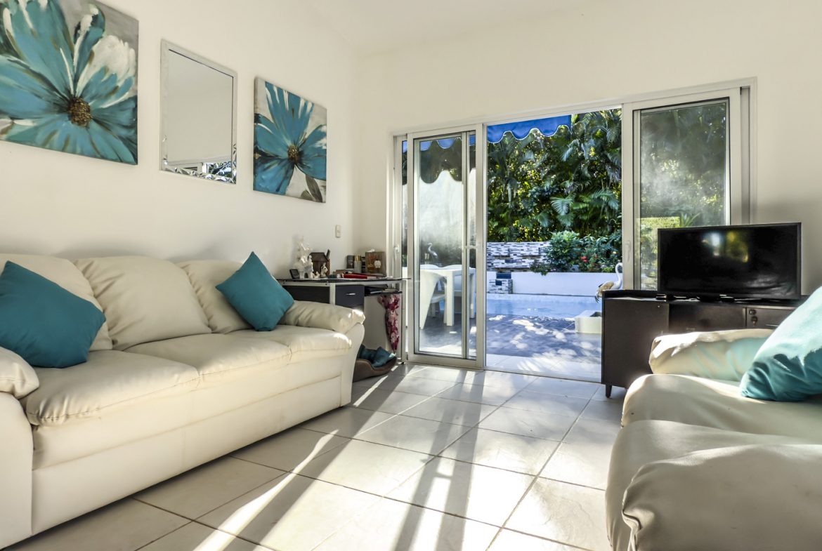 buyDRproperty Villa living room with white sofas, blue accents, and sliding glass doors to a private garden. Sosua Real Estate