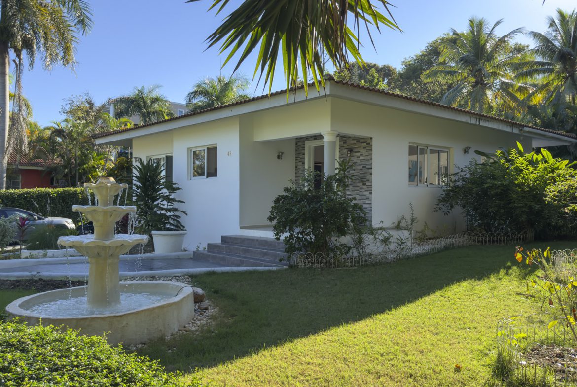buyDRproperty Colibri villa with white exterior, fountain, and lush tropical garden for sale. Sosua Real Estate