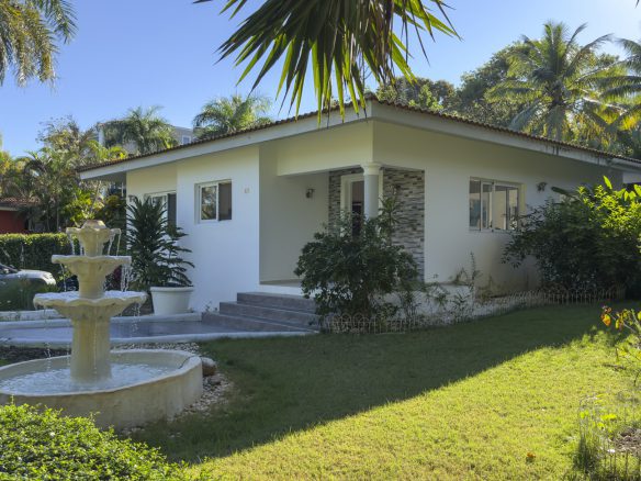 buyDRproperty Colibri villa with white exterior, fountain, and lush tropical garden for sale. Sosua Real Estate