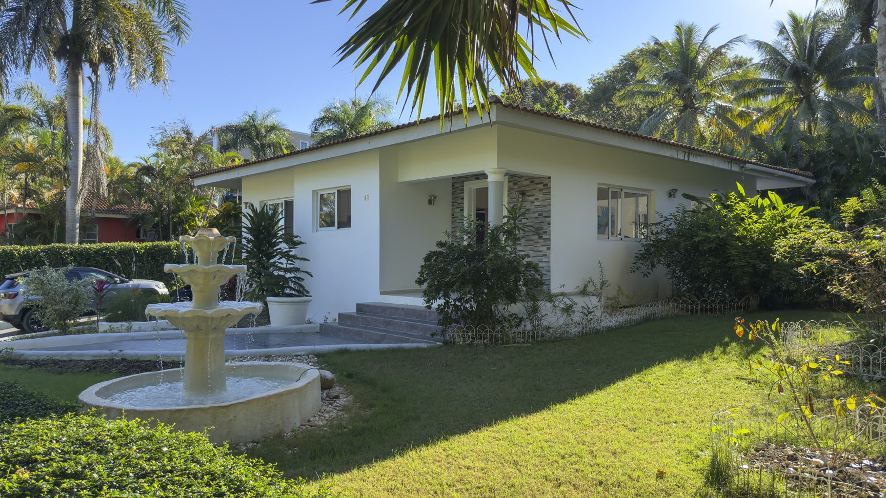 buyDRproperty Colibri villa with white exterior, fountain, and lush tropical garden for sale. Sosua Real Estate