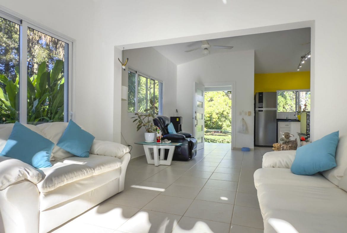 buyDRproperty Bright living space in a villa with white sofas and tile floors, leading to a garden view. Sosua Real Estate