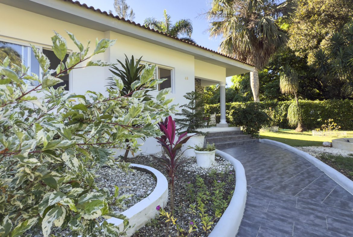 buyDRproperty Villa exterior with lush tropical garden, walkway, and small fountain. A peaceful oasis. Sosua Real Estate