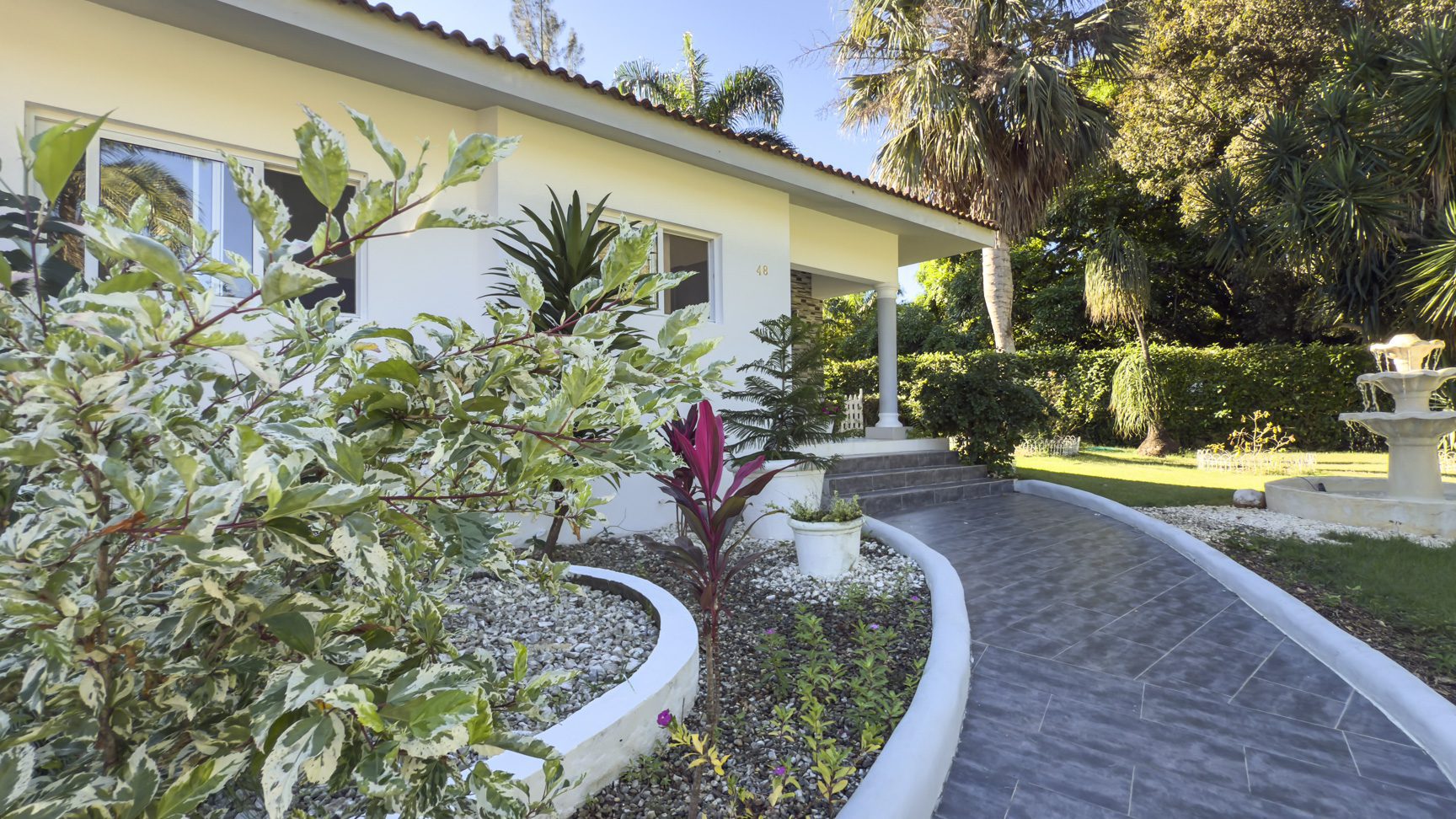 buyDRproperty Villa exterior with lush tropical garden, walkway, and small fountain. A peaceful oasis. Sosua Real Estate