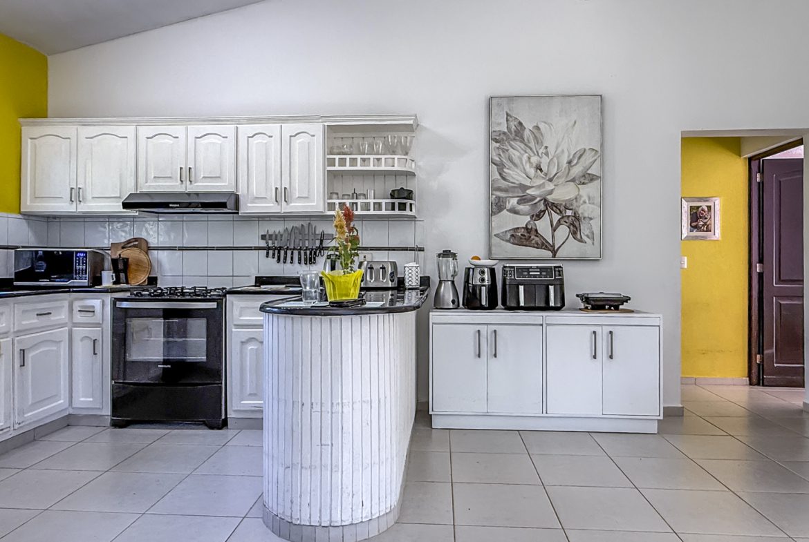 buyDRproperty Bright kitchen in a Colibri villa with white cabinets, black appliances, and yellow accent wall. Sosua Real Estate