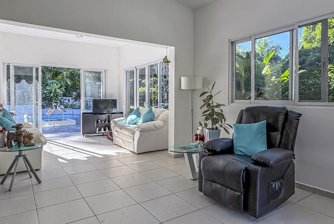 buyDRproperty Bright villa living room with garden view, white sofas, and black recliner. Sosua Real Estate