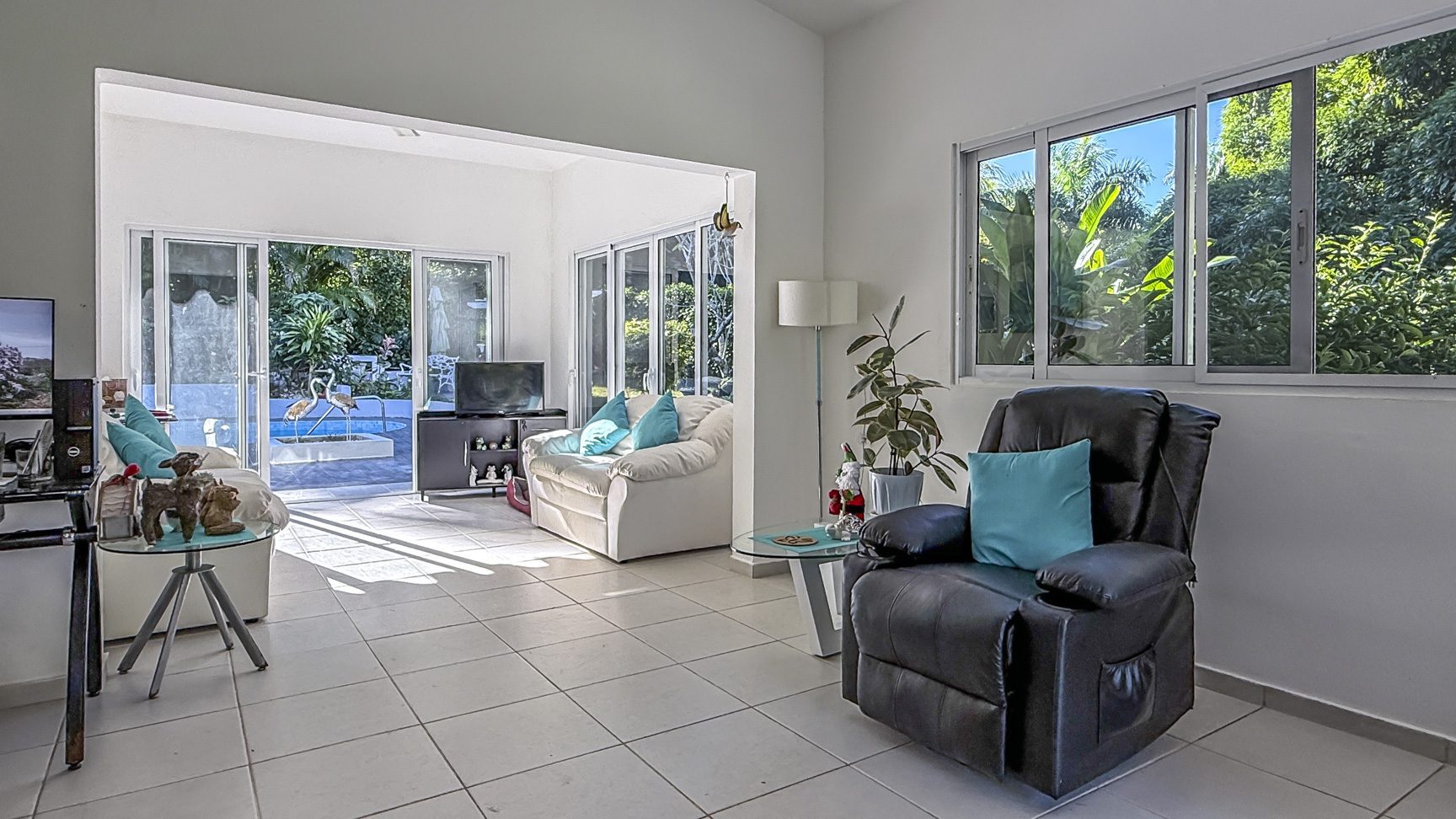 buyDRproperty Bright villa living room with garden view, white sofas, and black recliner. Sosua Real Estate